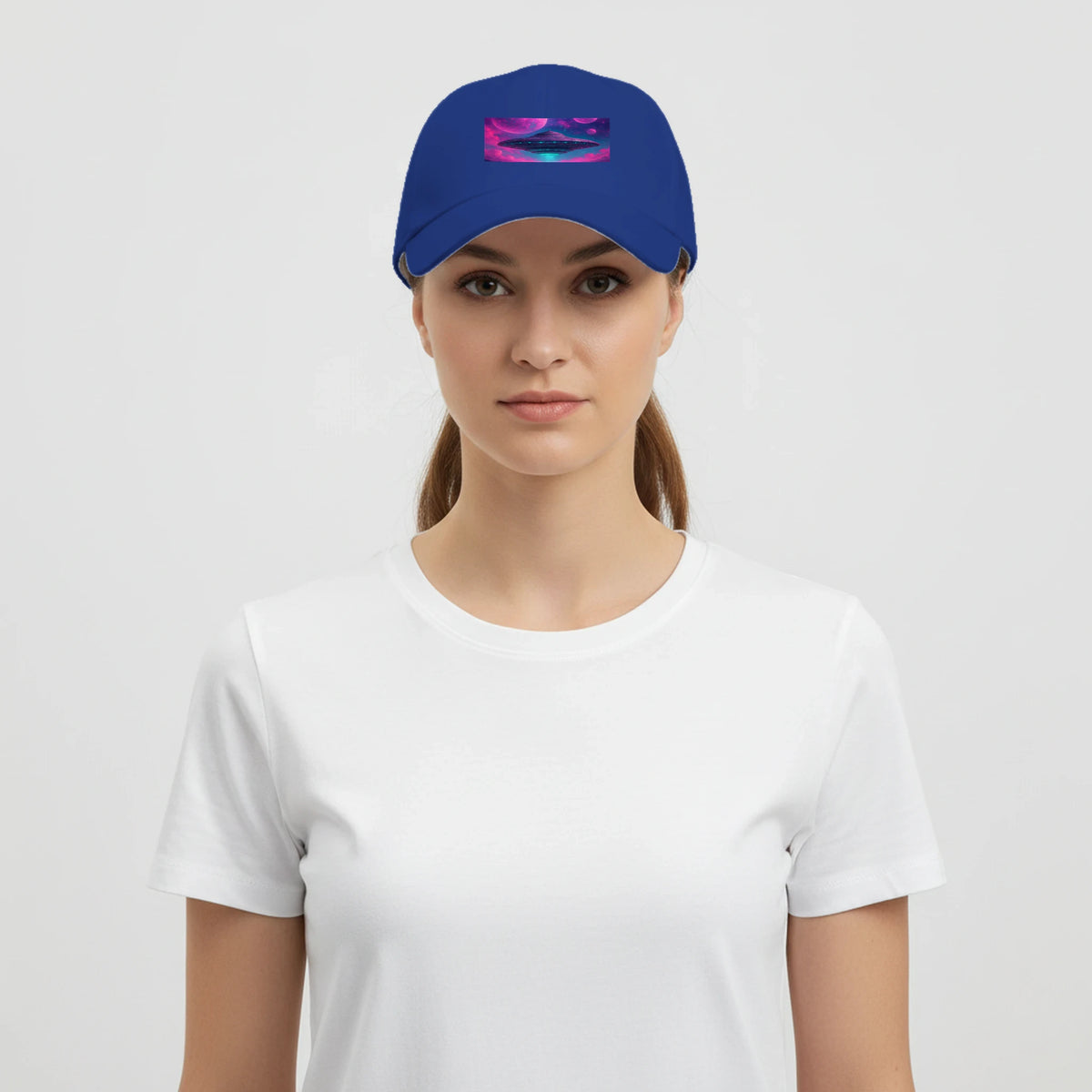 A woman wearing a royal blue baseball cap with a colorful abstract graphic on the front, paired with a plain white t-shirt, against a light gray background.